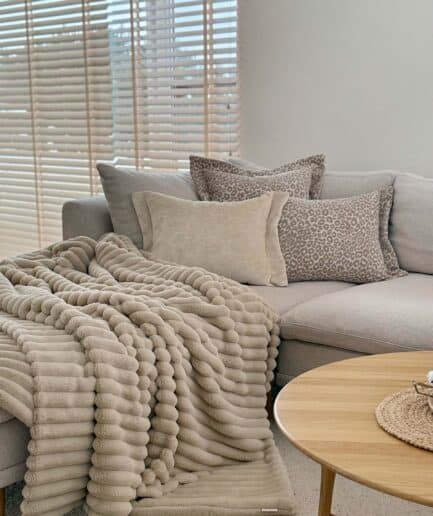 Dvipusis smėlio spalvos dirbtinio kailio pledas ant svetainės sofos.